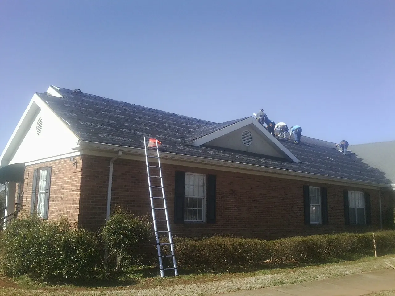 Crew tearing shingles off a brick ranch roof with a ladder set — Metal Roof Repair work by our crew in Shiloh