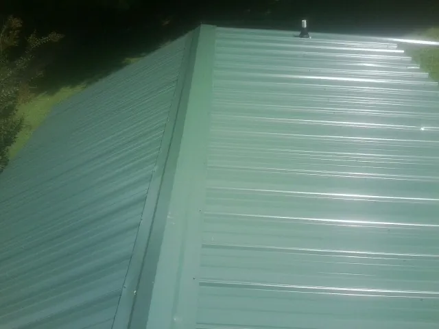 New green metal panels meeting at the ridge of a roof — Flat Roof Repair work by our crew in Shiloh